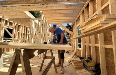Caucasian male builder on job site using saw to cut lumber for tiny home that he's framing