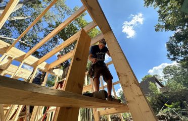 Caucasian male with cigarette in his mouth standing on support beam framing a tiny home