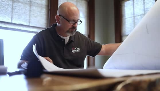 Caucasian man with glasses and goatee wearing blue Sineath shirt looking at architectural plans.